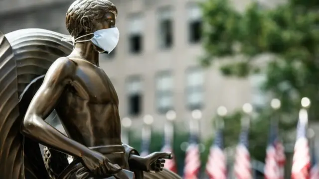 Statue wearing a face mask in front of US flags