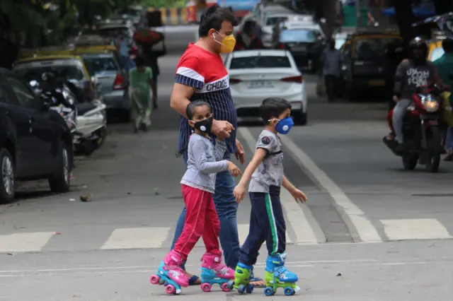 Children wearing face masks skate along a road in Mumbai, India on July 01, 2020.