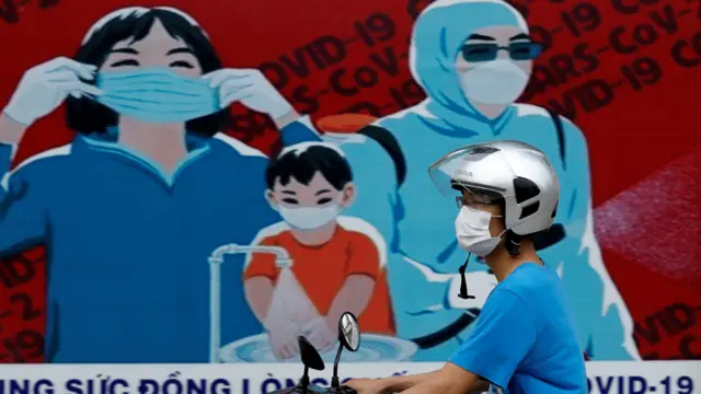 A man wears a protective mask as he drives past a banner promoting prevention against the coronavirus disease (COVID-19) in Hanoi, Vietnam, 31 July, 2020.