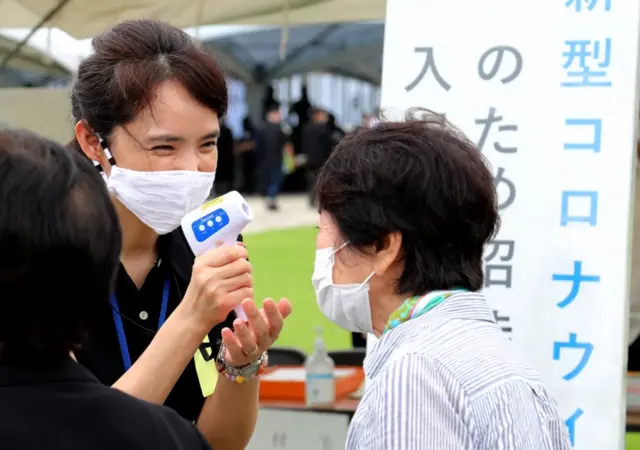 A resident has her temperature checked as she arrives at the Peace Memorial Park in Itoman, Okinawa, Japan