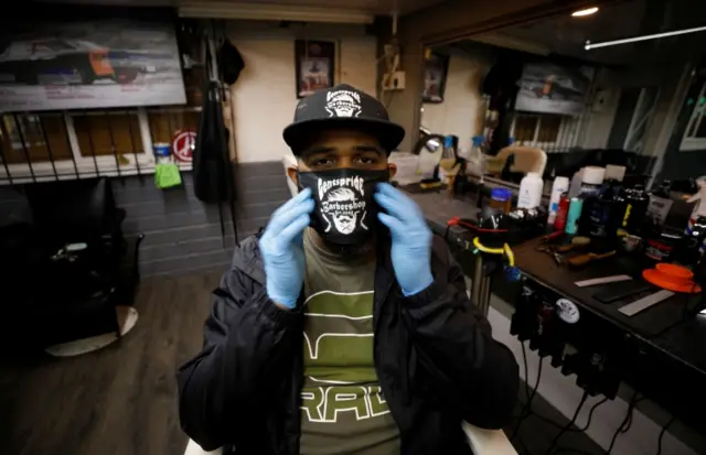 Adiel Sadie adjusts his face mask in his empty barbers shop, closed under the coronavirus lockdown in South Africa