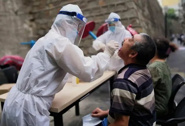 A medical worker in protective suit collects a swab