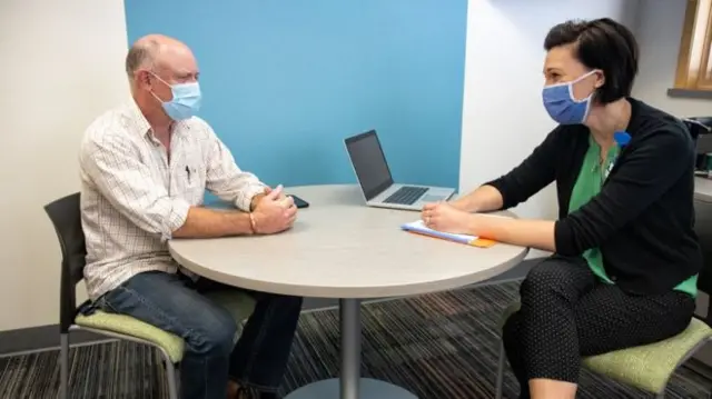 A man and woman wearing masks sit at a table