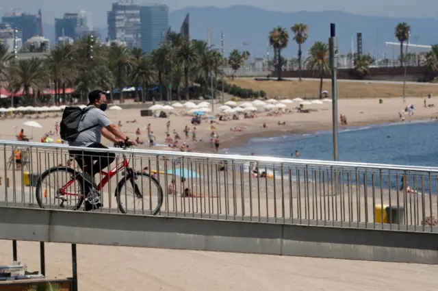 A man wearing a protective mask arrives by bike at Somorrostro beach in Barcelona