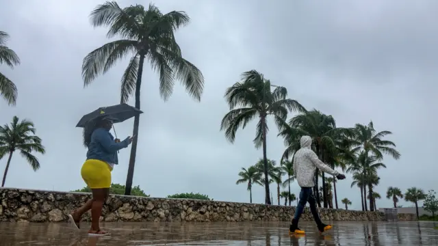 People walk in the wet streets as tropical storm Isaias is approaching East of the Miami shores, Miami beach, Florida.