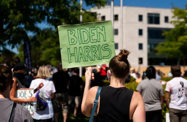 A woman holds a handmade sign that says "Biden Harris" in downtown as President Donald Trump makes a campaign stop at Mankato Regional Airport on August 17, 2020