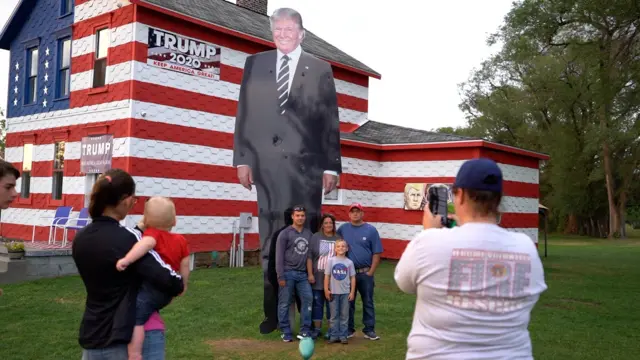 A family takes photos with a giant picture of Donald Trump