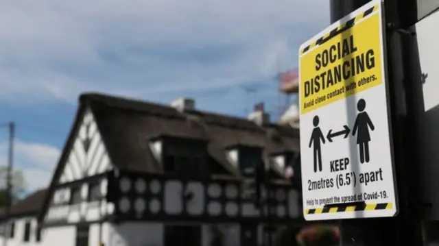 A sign reminds people to social distance near the Crown and Anchor pub