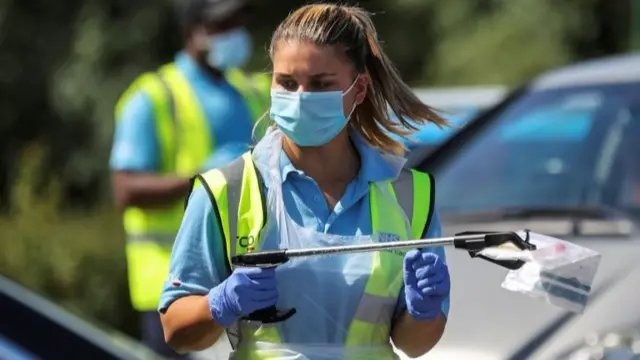 An NHS employee holds a sample at a testing centre near the Crown and Anchor pub