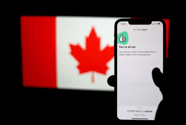 The COVID Alert application is displayed on a smart phone screen and the flag of Canada is displayed on a laptop screen in Vancouver, Canada on July 31, 2020