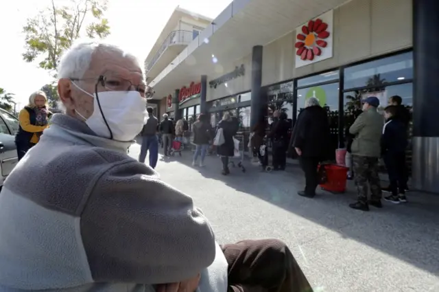 A man wearing a face mask sits outside a supermarket in Nice