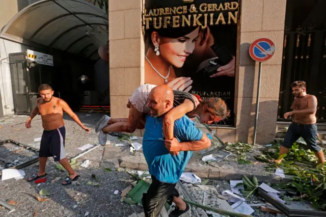 A man carries away an injured girl while walking through debris past in the Achrafiyeh district in the centre of Lebanon's capital Beirut on August 4