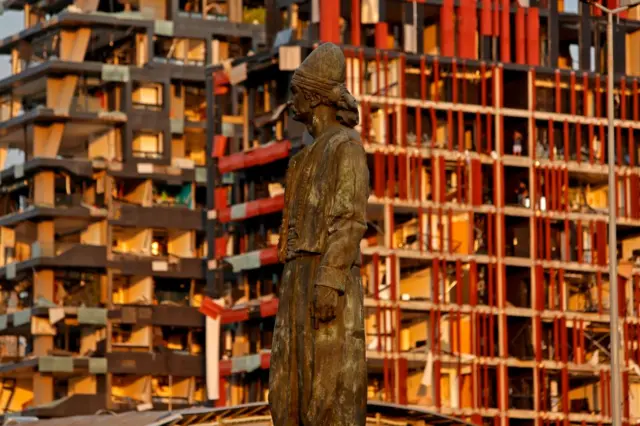 The statue of the Lebanese Emigrant stands intact in front of damaged buildings