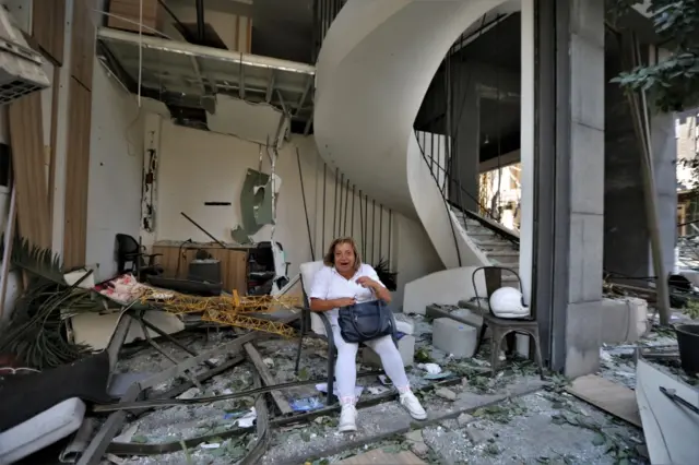 A  woman sits in front of a damaged building after the massive explosion in Beirut, Lebanon