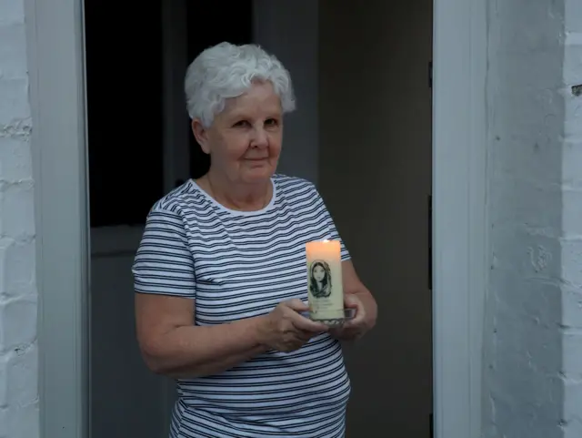 Ann Wilson holds a candle for John Hume outside her home