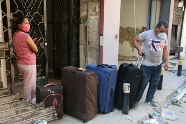 People stand with their belongings as they evacuate their damaged house, following Tuesday"s blast in Beirut"s port area