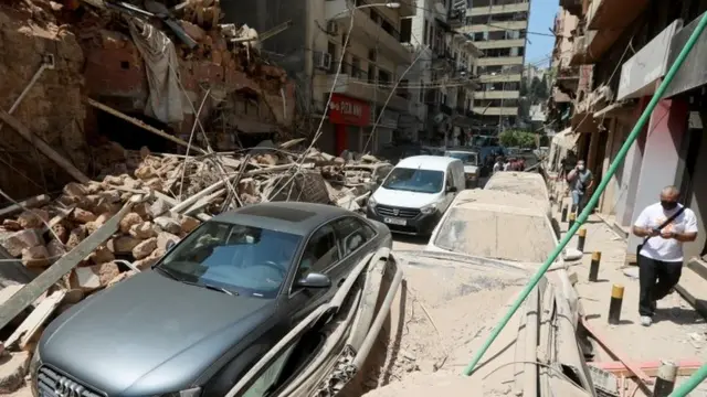 Vehicles driving past damaged buildings and cars