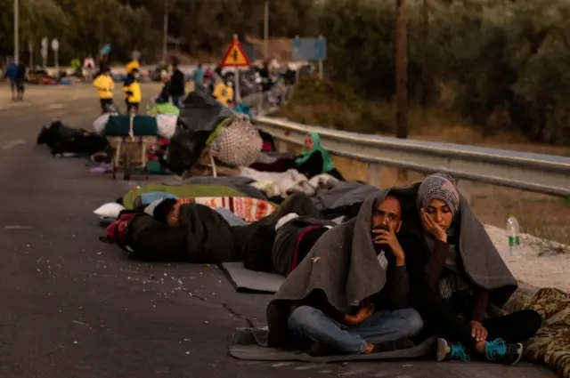 A couple sits covered with a blanket as refugees and migrants camp on a road following a fire at the Moria camp on the island of Lesbos, Greece, September 10, 2020.