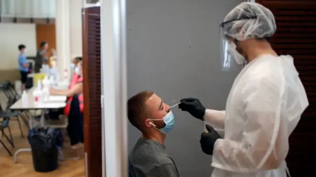 A health worker, wearing a protective suit and a face mask, prepares to administer a nasal swab to a patient at a testing site for the coronavirus disease