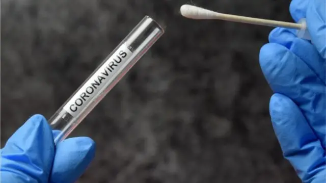 A file image of a test tube saying 'coronavirus' and a cotton bud being placed inside it