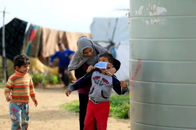 Syrian refugee in southern Lebanon tries to put mask on child