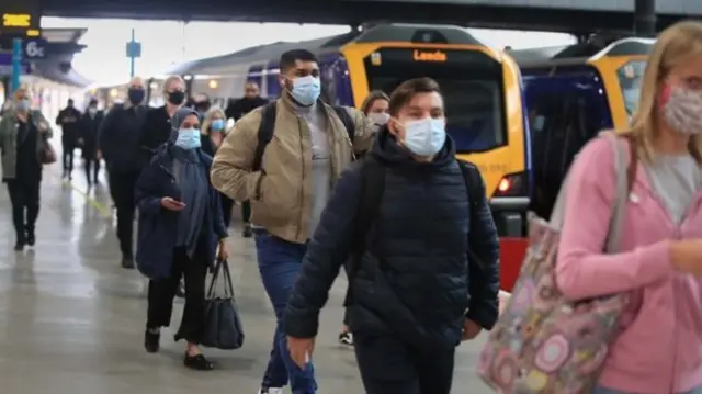 Passengers wear masks as they leave a platform