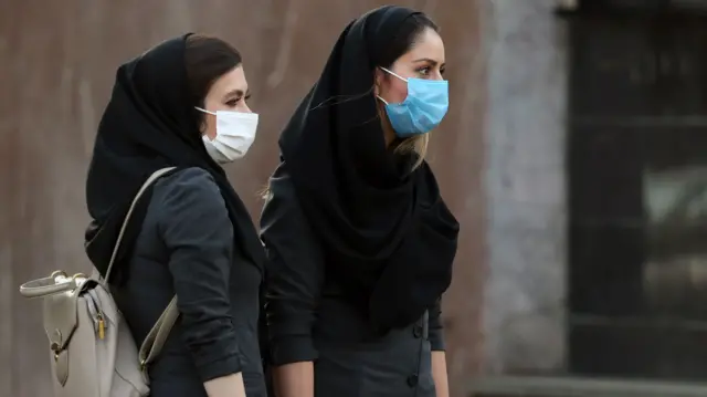 Iranian women wear face masks while waiting for a taxi in a street in Tehran, Iran