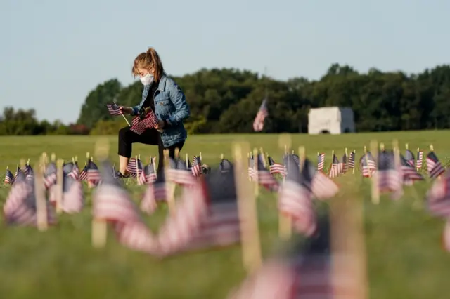 A volunteer places American flags representing some of the 200,000 lives lost in the US