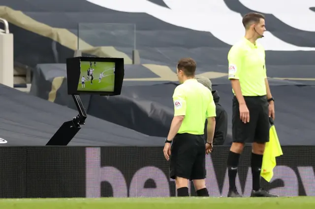 Referee Peter Bankes looks at the pitchside monitor