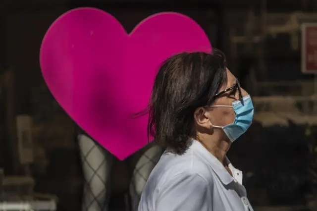 A woman in a face mask walks past a heart sign