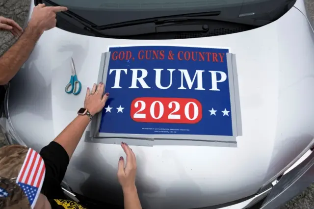 A woman attaches a Trump 2020 sign to a vehicle in Cincinnati, Ohio during a car parade, 12 September