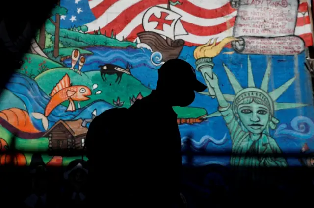 Man in a mask walks past a mural in New York