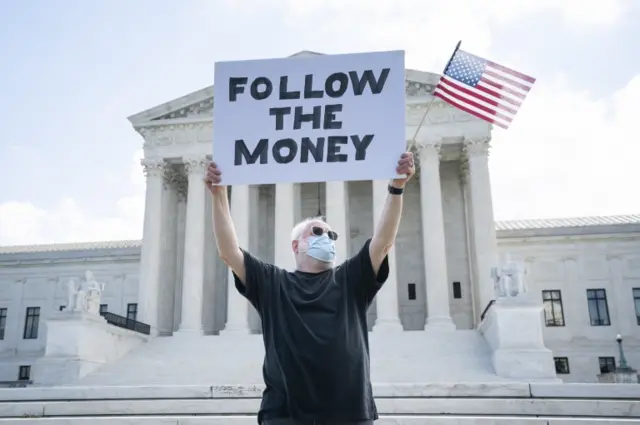 A protester outside the Supreme Court holds a sign saying "follow the money"