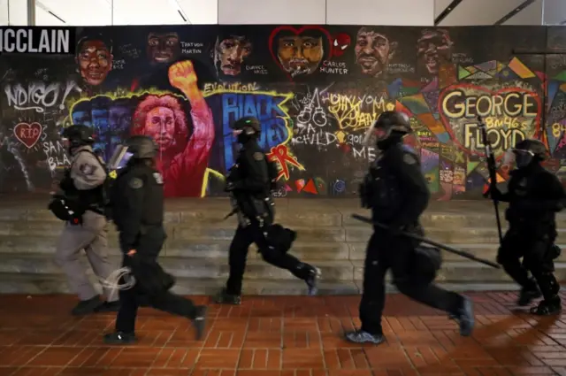 Police officers run past graffiti during a protest against police violence and racial inequality in Portland, Oregon, on September 27, 2020.