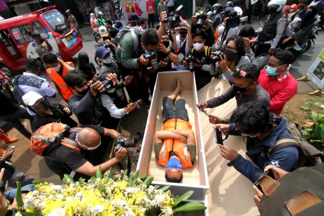 A man, caught not wearing a face mask in public lies in a mock coffin while members of the public and the media take pictures as part of punishment by local authorities and enforced by local police, in Jakarta, on 3 September, 2020