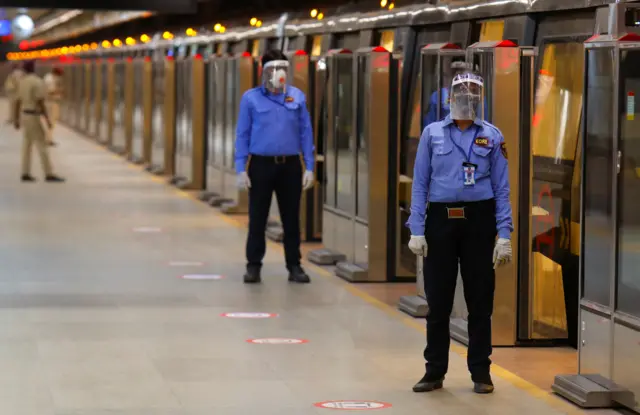 Security guards wearing face masks and shields stand on a Delhi metro train platform, on the first day of the restart of their operations, amidst the spread of coronavirus disease