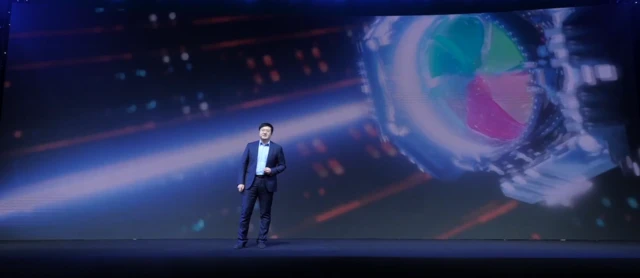 Dr Liu Xianrong, the Chief Scientist of Hisense Laser Display, stands on the stage at CES with laser graphics on the screen behind him