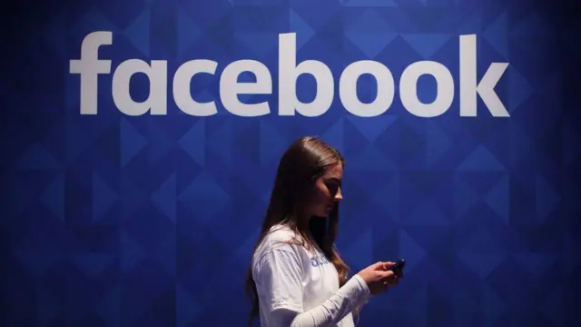 A woman walks in front of the Facebook logo