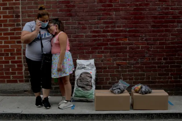 A mother made jobless waits with her child after picking up a grocery handout in Massachusetts