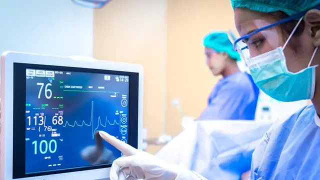 Doctors in a hospital ICU pointing at a screen