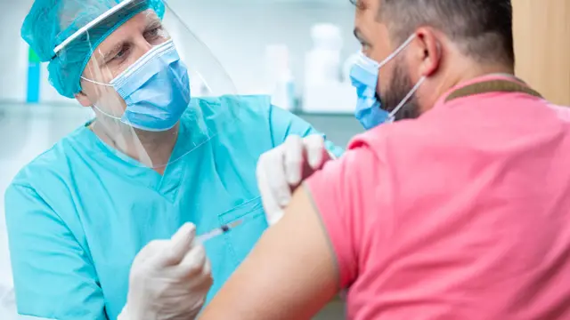 Medic administers jab to man in pink shirt