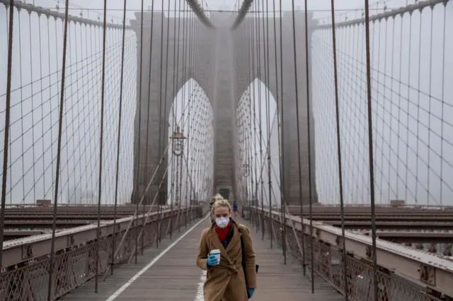 Woman wearing a mask walks across the Brooklyn Bridge