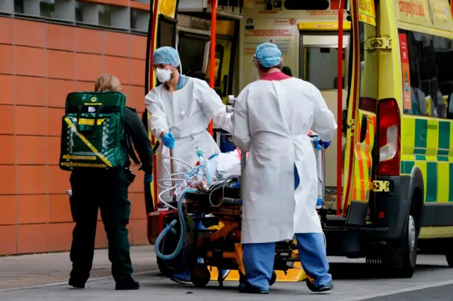 NHS staff in full PPE unload patient from ambulance