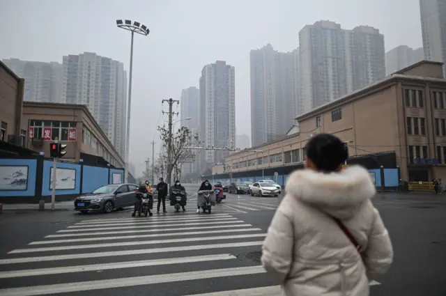 People wait to cross a street in front of the closed Huanan Seafood wholesale market in Wuhan, China's central Hubei province on January 23, 2021
