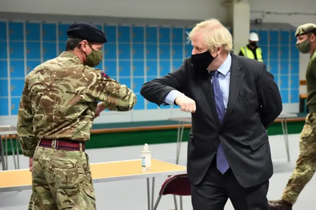 Prime Minister Boris Johnson elbow bumps a member of the military as he meets troops setting up a vaccination centre in the Castlemilk district of Glasgow on his one day visit to Scotland