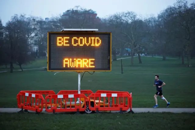 A man jogs past a public health information sign on Primrose Hill, London