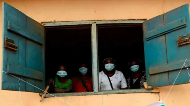 People wearing facemasks stand at a window