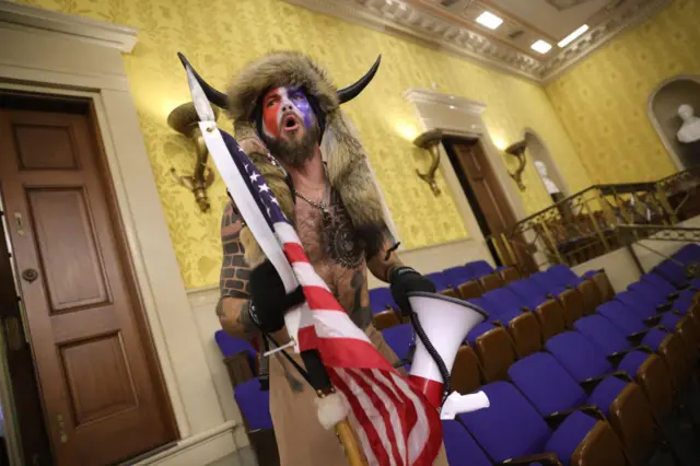 A protester screams "Freedom" inside the Senate chamber wearing a fur hat, horns and with a naked torso, carrying an Amreican flag