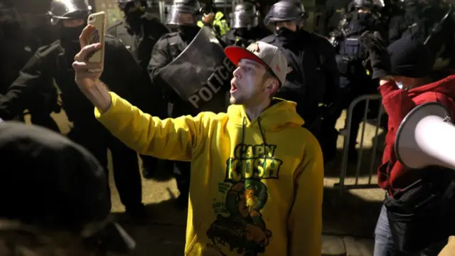 Man taking a selfie in front of police in riot gear