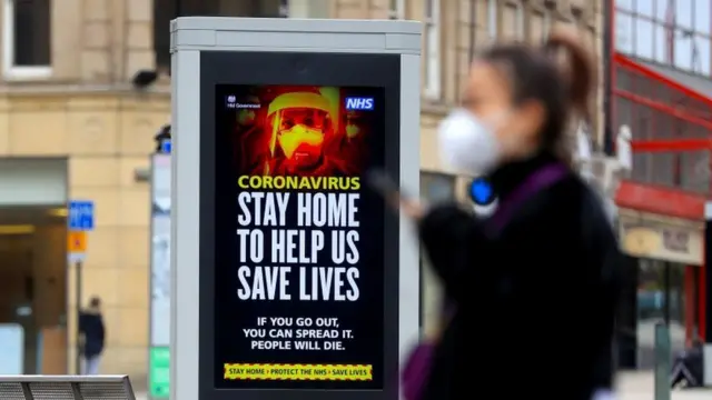 A woman walks past an information screen displaying Covid advice